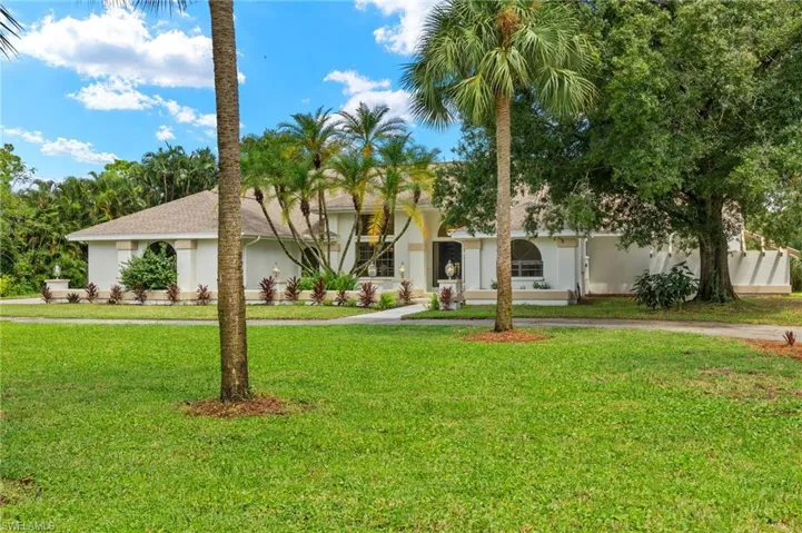 View of front of house with stucco siding, a front lawn, and curved driveway