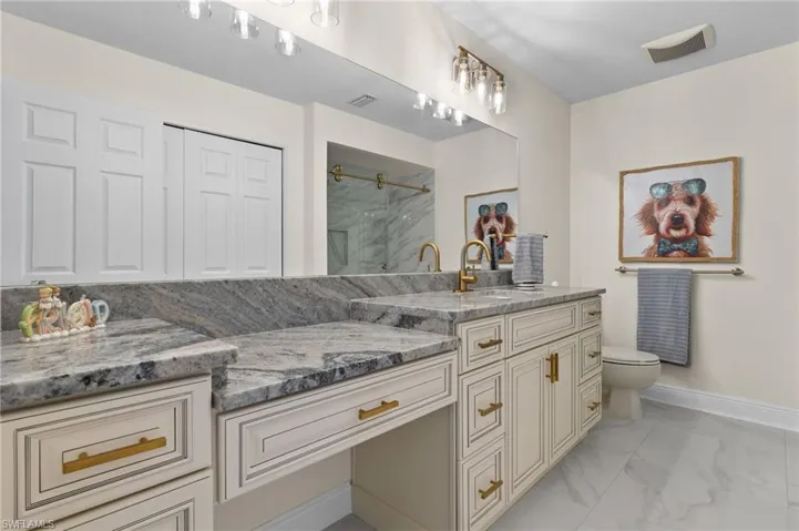 Bathroom featuring baseboards, toilet, vanity, a marble finish shower, and marble finish floor