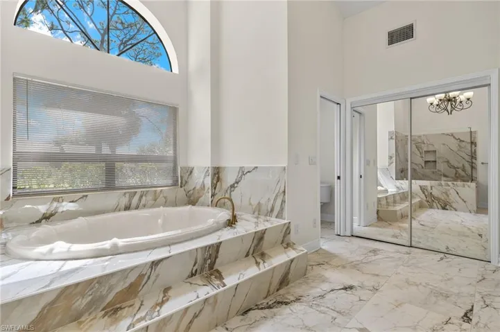 Bathroom featuring visible vents, marble finish floor, a high ceiling, and a garden tub