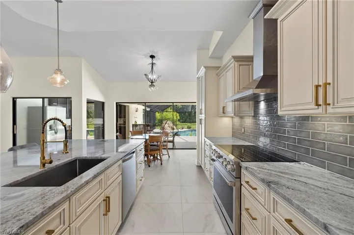 Kitchen with stainless steel appliances, a sink, cream cabinets, and wall chimney range hood