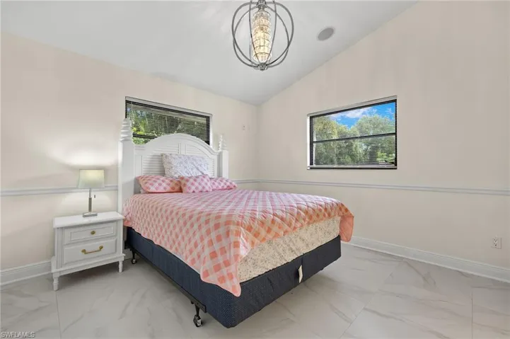 Bedroom with multiple windows, marble finish floor, baseboards, and lofted ceiling