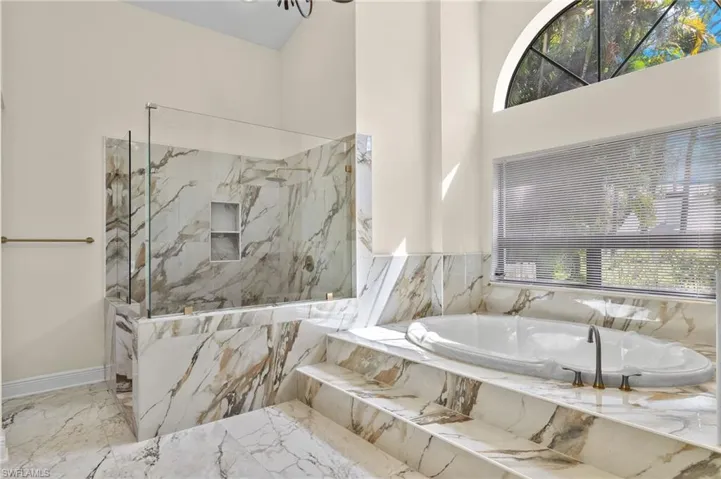 Bathroom featuring a bath, baseboards, a towering ceiling, a marble finish shower, and marble finish floor