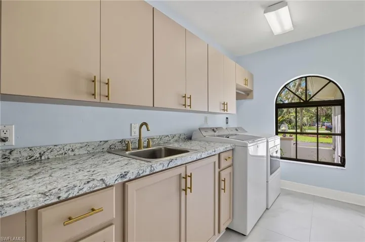 Laundry area with marble finish floor, a sink, washer and dryer, baseboards, and cabinet space