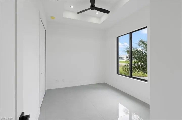 Unfurnished room featuring plenty of natural light, ceiling fan, and a tray ceiling
