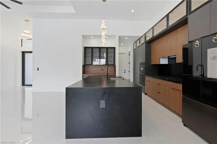 Kitchen featuring hanging light fixtures, sink, black refrigerator, ceiling fan, and a center island with sink
