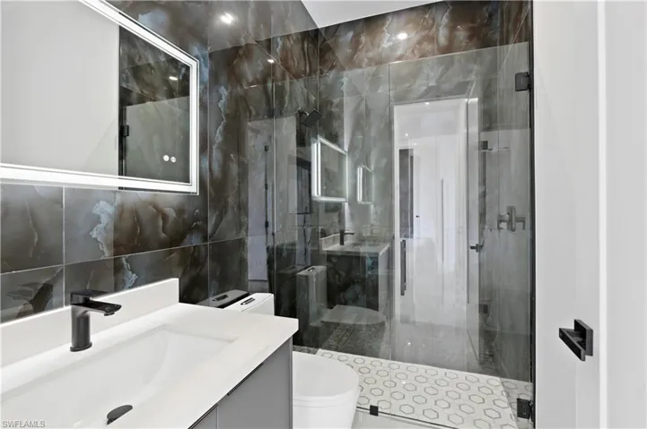 Bathroom with vanity, toilet, walk in shower, and tile walls
