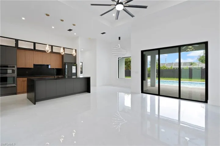 Kitchen with decorative light fixtures, a center island with sink, ceiling fan, decorative backsplash, and stainless steel double oven