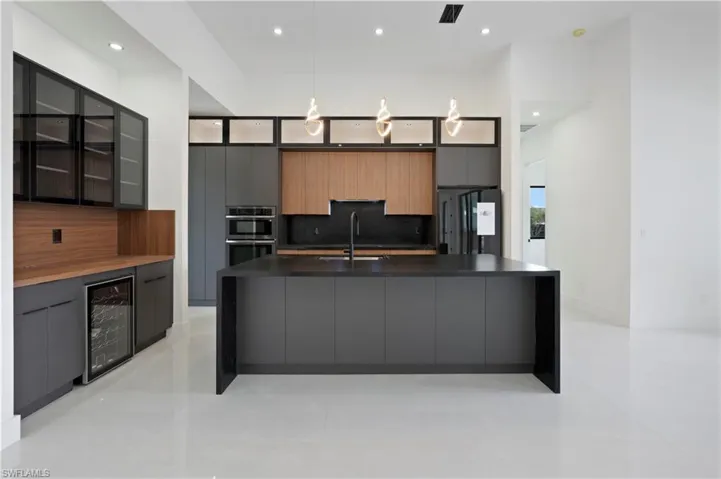Kitchen with fridge, wine cooler, sink, hanging light fixtures, and a large island