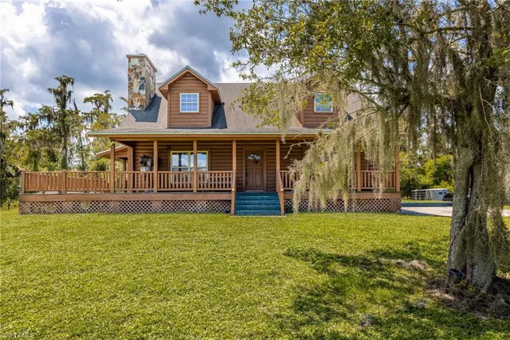 Log home featuring a shingled roof, a front yard, covered porch, and a chimney