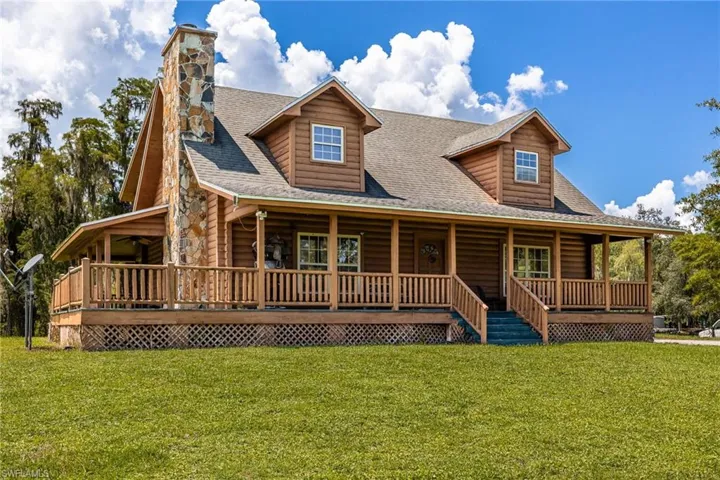 Log cabin with a shingled roof, a porch, a front yard, and log veneer siding