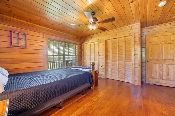 Bedroom featuring wooden walls, two closets, hardwood / wood-style floors, ceiling fan, and wood ceiling