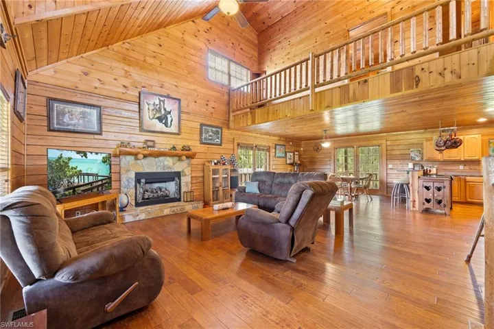 Living room featuring a vaulted wooden ceiling, a fireplace, light wood finished floors, and wood walls