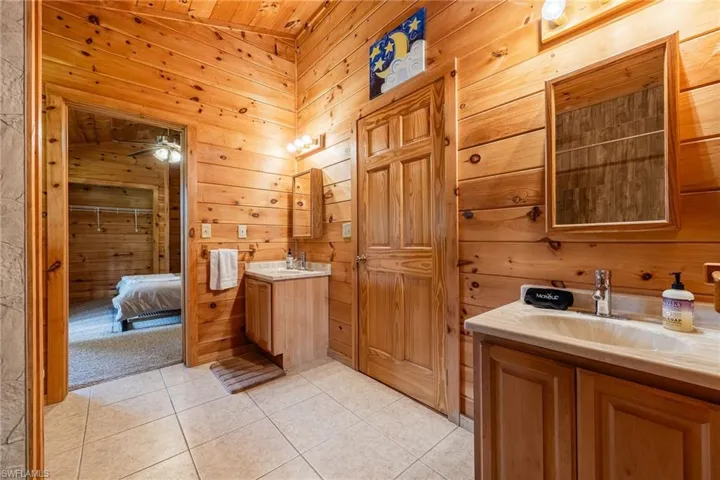 Ensuite bathroom with wooden walls, two vanities, light tile patterned floors, and wood ceiling