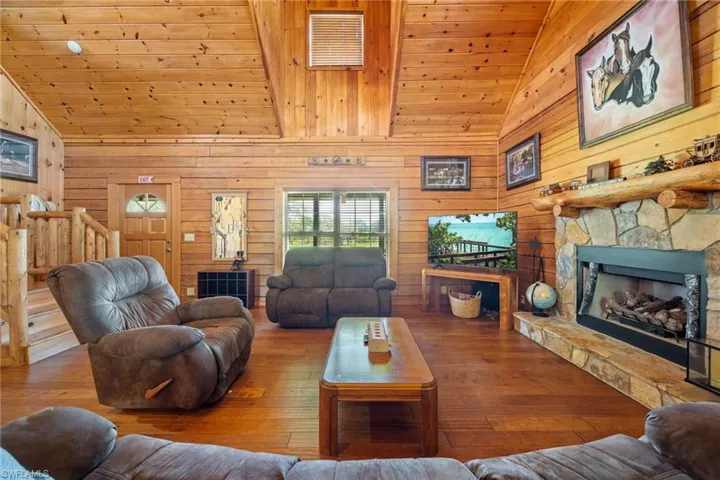 Living room with a stone fireplace, wood walls, a vaulted wooden ceiling, and wood-type flooring