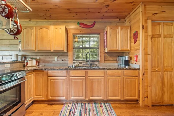 Kitchen with stainless steel range with electric cooktop, dark stone countertops, light wood-style floors, wood ceiling, and wooden walls