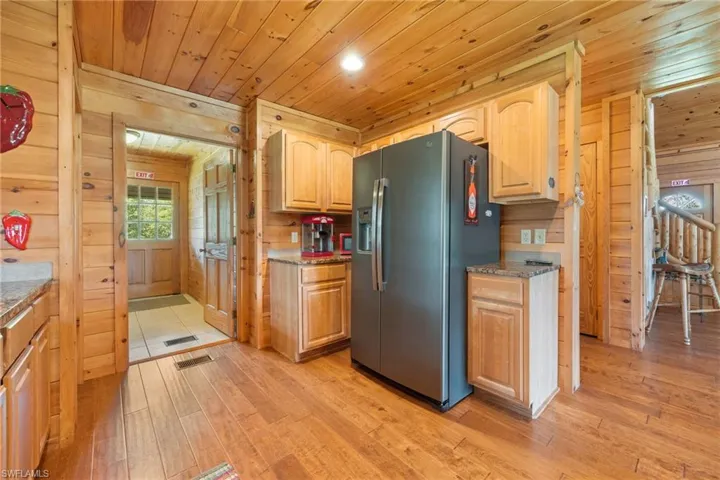 Kitchen with wood walls, stainless steel fridge with ice dispenser, light wood-style flooring, wood ceiling, and light stone counters