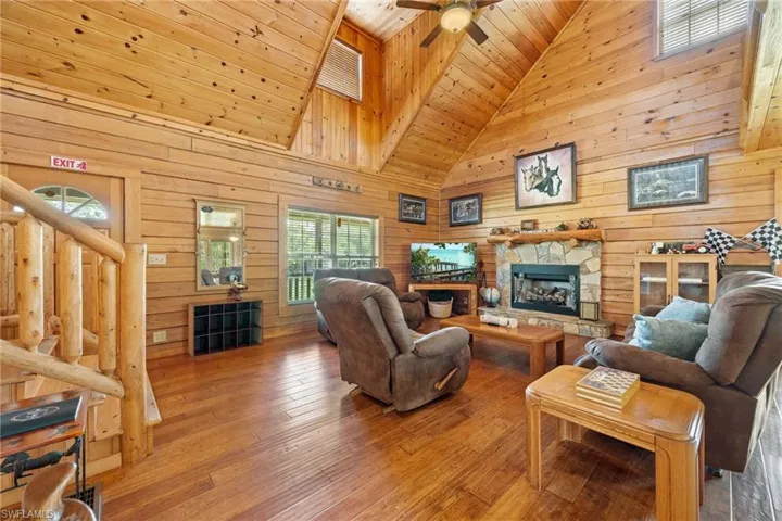 Living area with wood walls, wood-type flooring, a fireplace, a vaulted wooden ceiling, and a ceiling fan