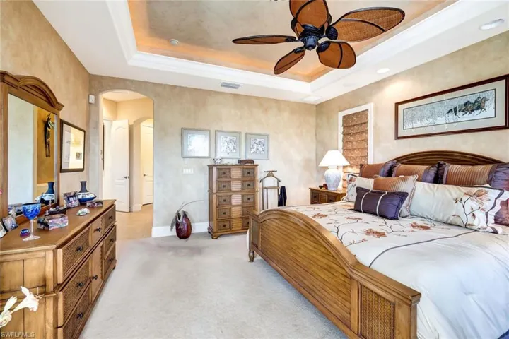 Bedroom featuring a raised ceiling, arched walkways, light colored carpet, ceiling fan, and crown molding