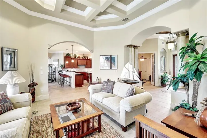 Living area with arched walkways, coffered ceiling, crown molding, a towering ceiling, and beam ceiling