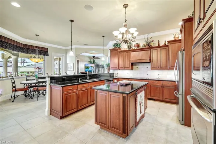 Kitchen featuring brown cabinetry, a peninsula, stainless steel appliances, pendant lighting, and a chandelier