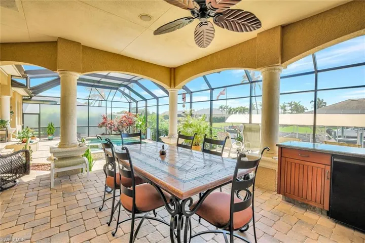 View of patio with glass enclosure, a sunroom, a ceiling fan, and outdoor dining area
