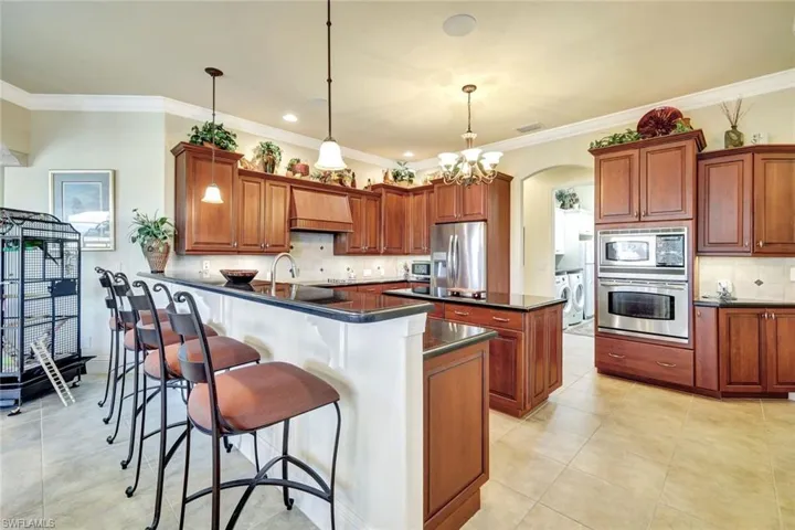 Kitchen featuring ornamental molding, hanging light fixtures, brown cabinets, stainless steel appliances, and a kitchen breakfast bar