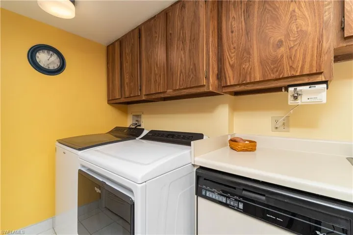 Clothes washing area featuring washing machine and clothes dryer, light tile patterned floors, and cabinets