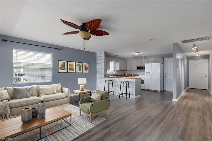 Living area with a ceiling fan, healthy amount of natural light, dark wood-style floors, and a textured ceiling
