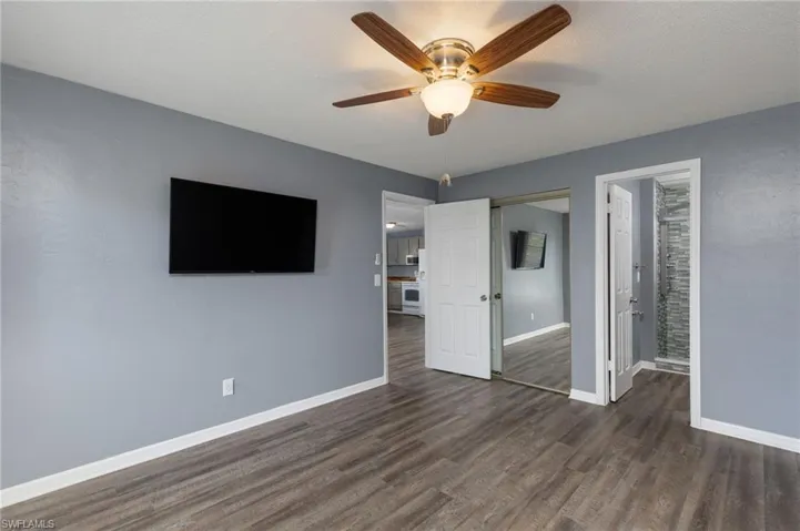 Unfurnished bedroom featuring dark wood-type flooring, ceiling fan, a closet, and ensuite bathroom