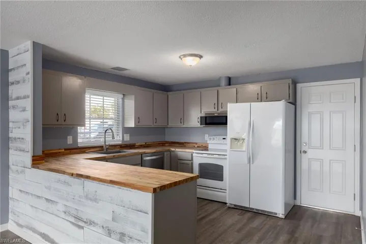 Kitchen with wood counters, stainless steel appliances, a peninsula, dark wood-style floors, and a textured ceiling