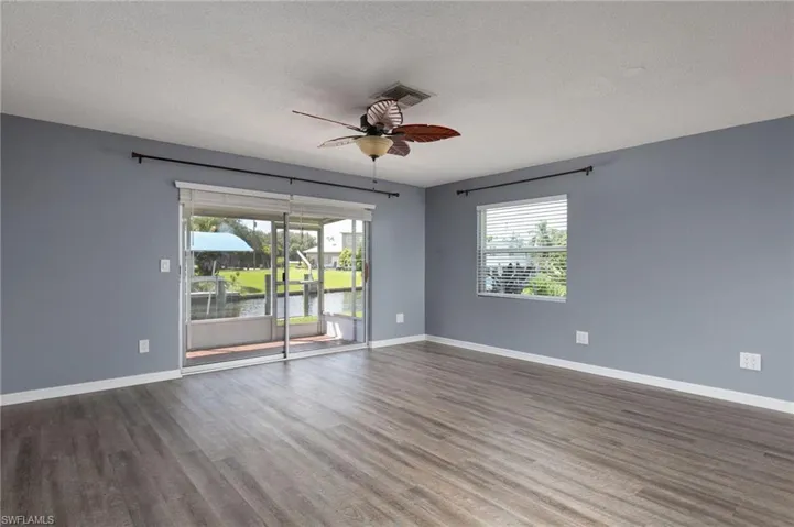 Empty room featuring plenty of natural light, a ceiling fan, a water view, a textured ceiling, and dark wood finished floors