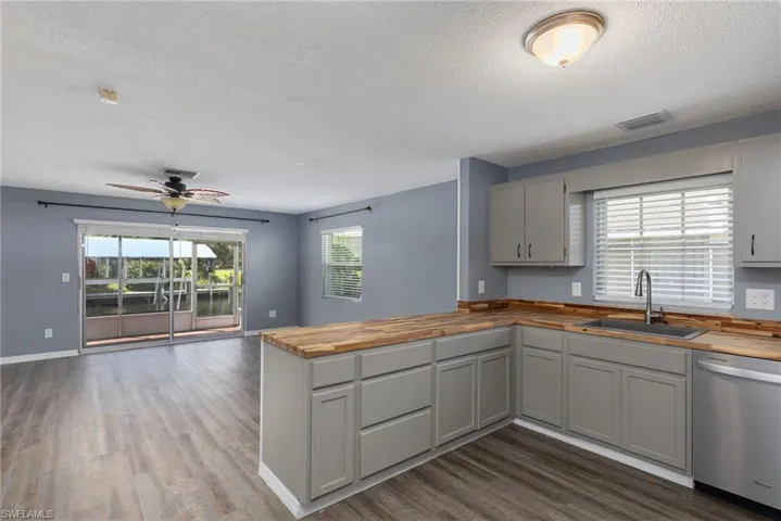 Kitchen with butcher block counters, stainless steel dishwasher, a peninsula, a ceiling fan, and a textured ceiling