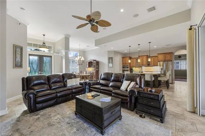 Living room with french doors, ceiling fan with notable chandelier, a wealth of natural light, and ornamental molding