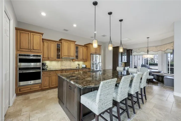 Kitchen with a breakfast bar, stainless steel appliances, decorative light fixtures, dark stone countertops, and a large island