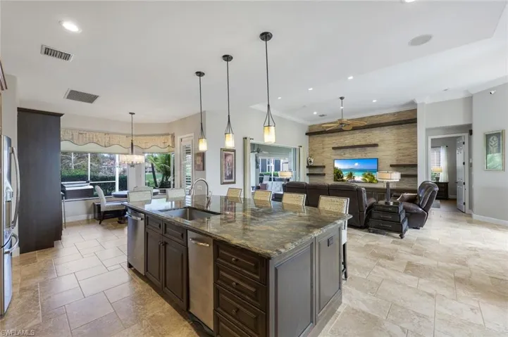 Kitchen with ceiling fan, sink, dark stone countertops, pendant lighting, and a kitchen island with sink