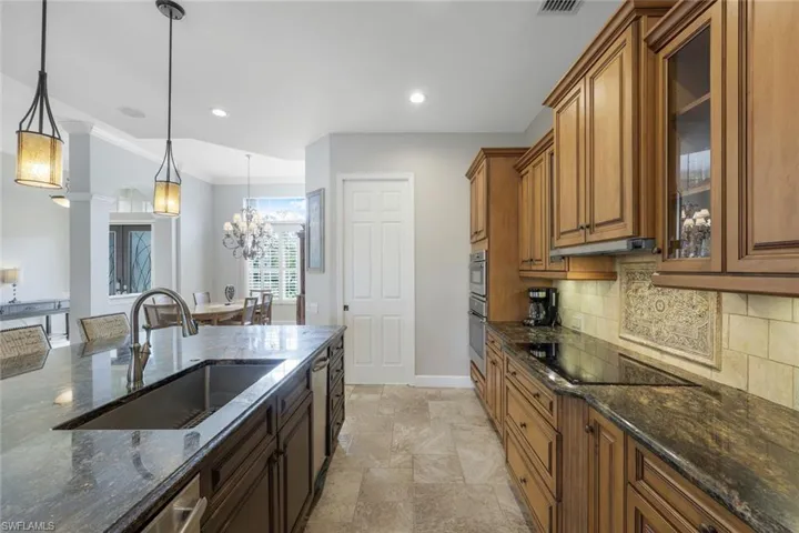 Kitchen featuring black electric cooktop, sink, pendant lighting, an inviting chandelier, and dark stone countertops
