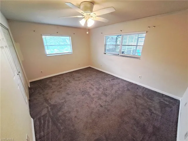 Unfurnished bedroom with dark colored carpet, ceiling fan, and a closet