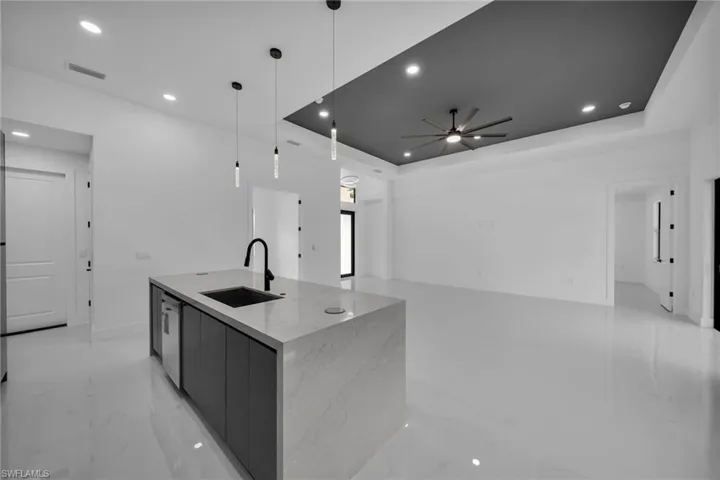 Kitchen with ceiling fan, a tray ceiling, hanging light fixtures, sink, and a kitchen island with sink