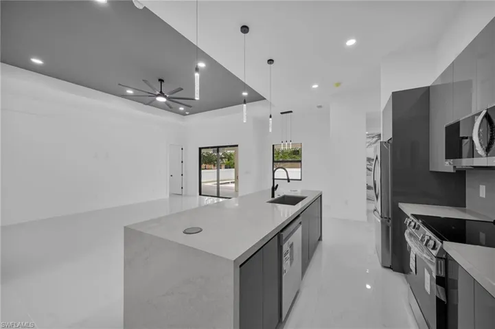 Kitchen with appliances with stainless steel finishes, sink, decorative light fixtures, a large island, and ceiling fan