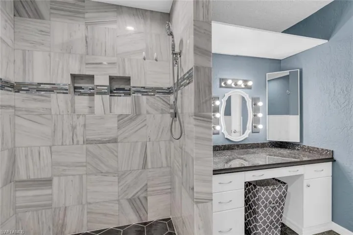 Full bathroom featuring a tile shower, vanity, and a textured wall