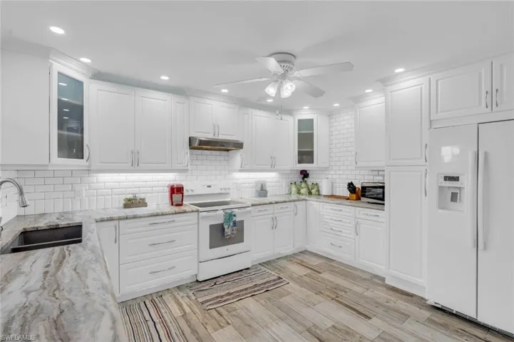 Kitchen featuring white appliances, white cabinetry, a ceiling fan, backsplash, and glass insert cabinets