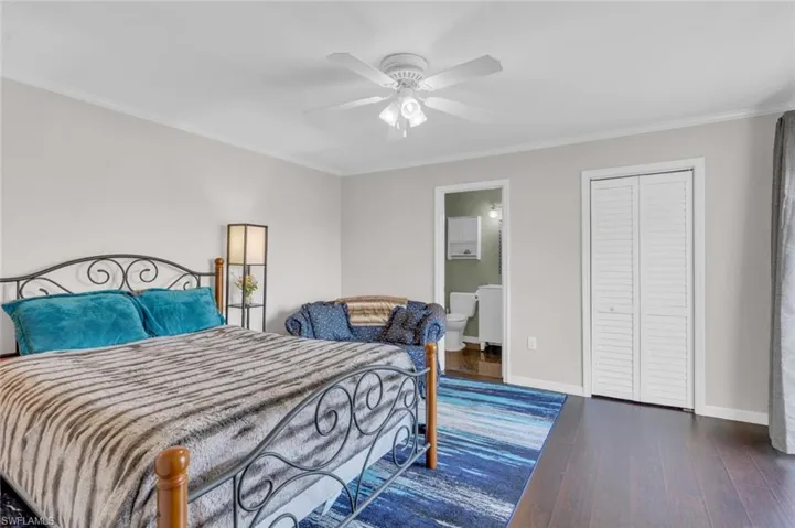 Bedroom with wood finished floors, crown molding, connected bathroom, a ceiling fan, and a closet