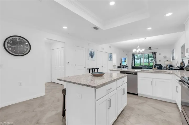 Kitchen with white cabinetry, a kitchen island, an inviting chandelier, light stone countertops, and appliances with stainless steel finishes
