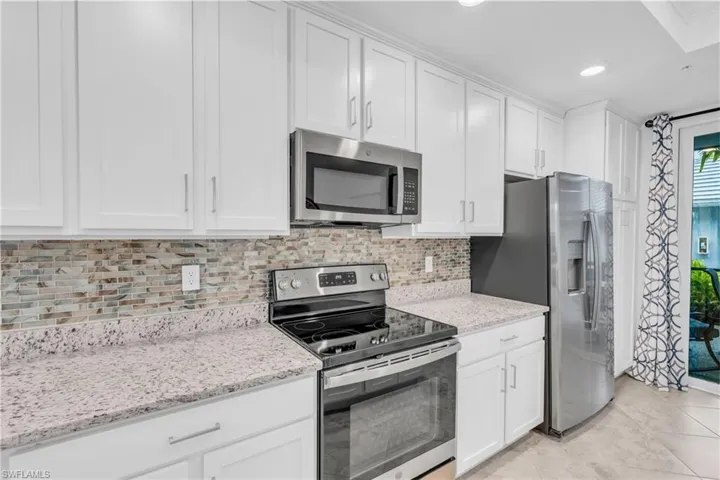 Kitchen featuring white cabinetry, light tile patterned floors, stainless steel appliances, light stone countertops, and decorative backsplash