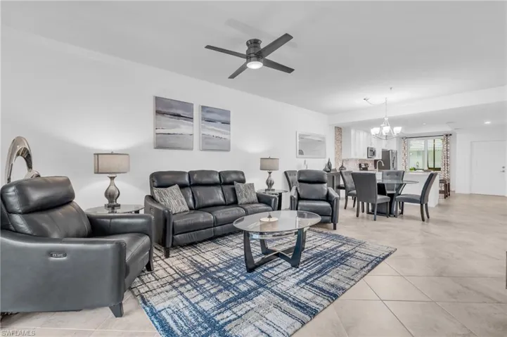 Living room with ceiling fan with notable chandelier, light tile patterned floors, and crown molding