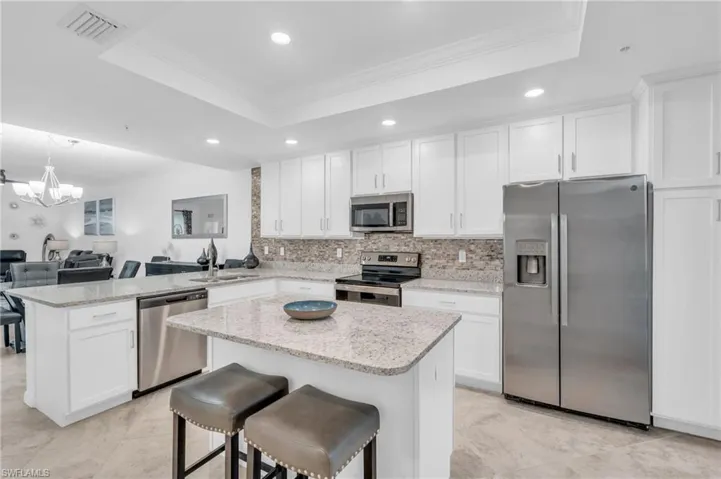 Kitchen featuring stainless steel appliances, a notable chandelier, white cabinetry, sink, and a raised ceiling