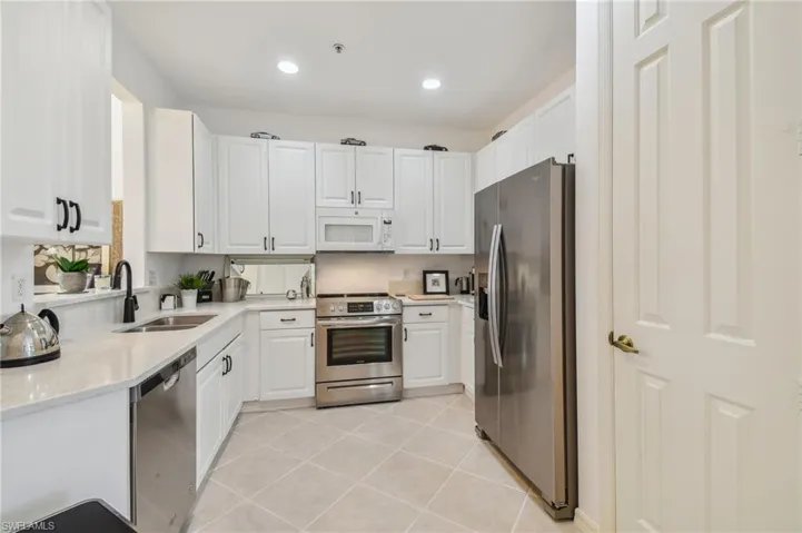 Kitchen with appliances with stainless steel finishes, white cabinetry, light tile patterned floors, and sink
