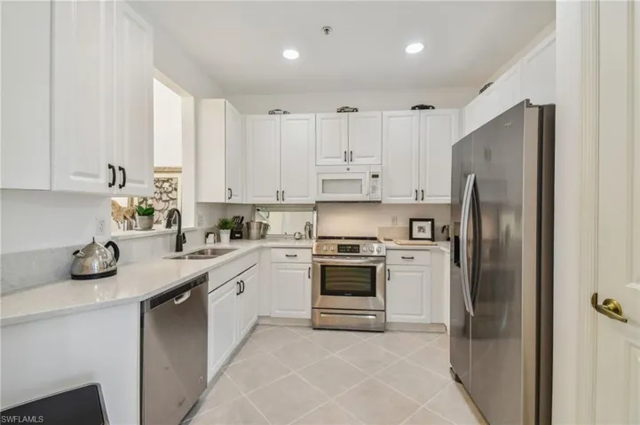 Kitchen with appliances with stainless steel finishes, light stone countertops, white cabinetry, sink, and light tile patterned flooring