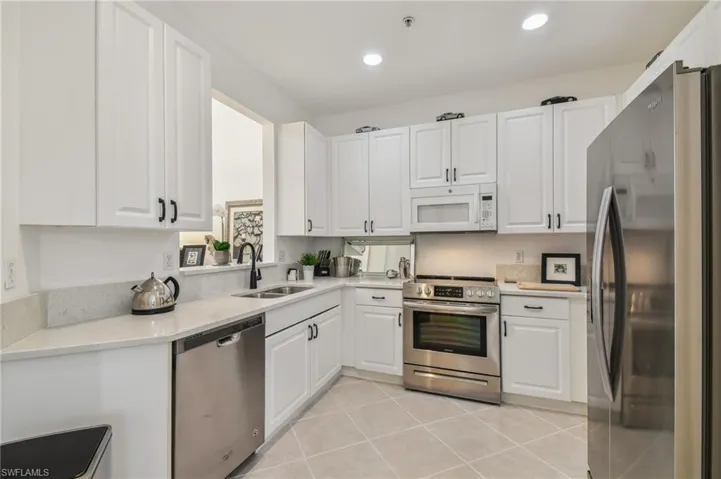 Kitchen with white cabinets, appliances with stainless steel finishes, light tile patterned floors, and sink