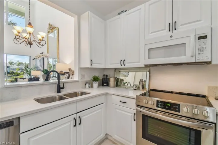 Kitchen featuring a notable chandelier, hanging light fixtures, stainless steel appliances, sink, and white cabinetry
